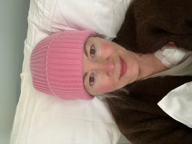 Dr. Lange snaps a selfie while undergoing treatment. She is smiling softly and wearing a light pink beanie that brings out the pink in her cheeks.