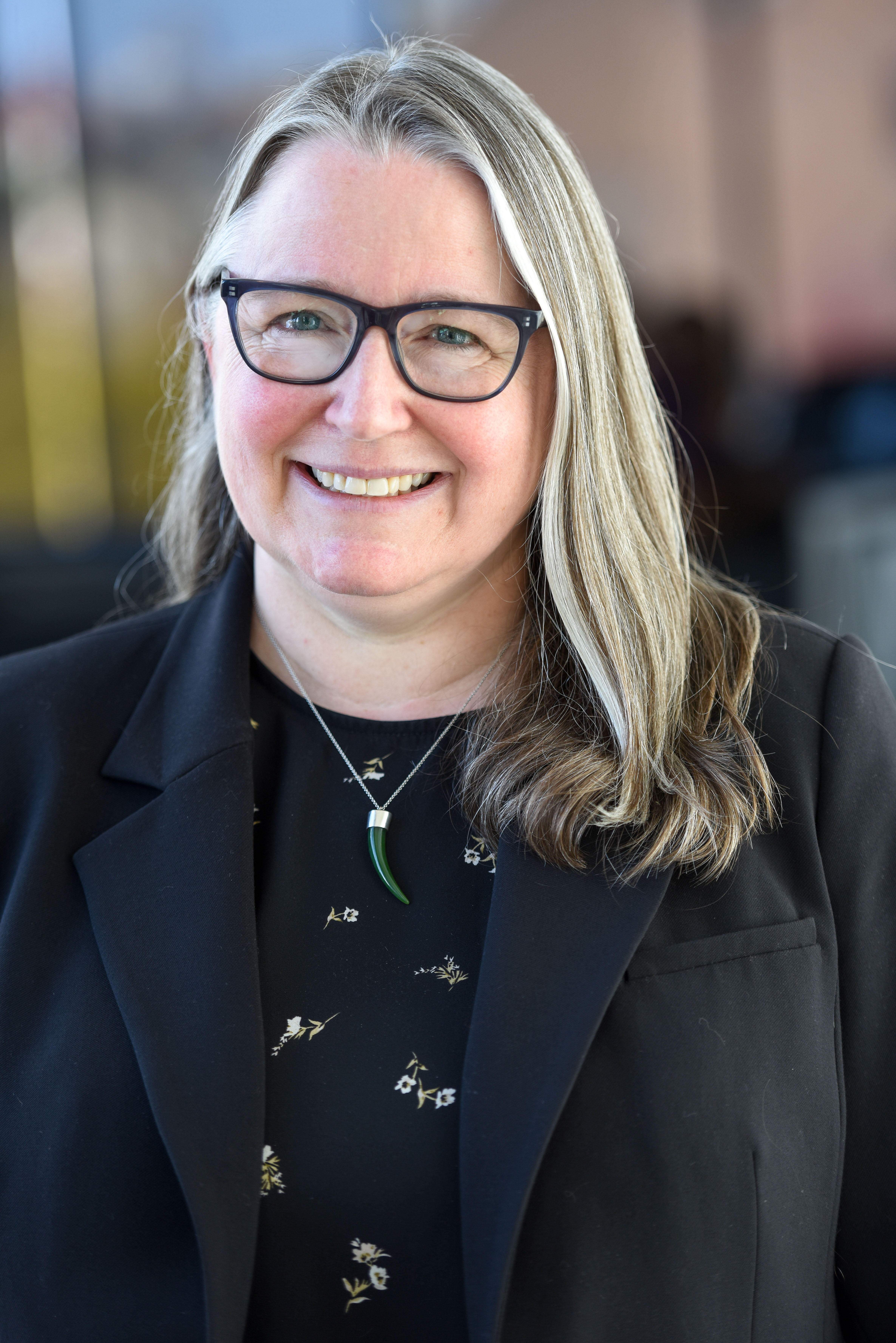 Dr. Rebekah Pratt poses for a portrait. Her grayish brown hair is pulled to the right side, and she is wearing black framed glasses that coordinate with her black top and black blazer. 